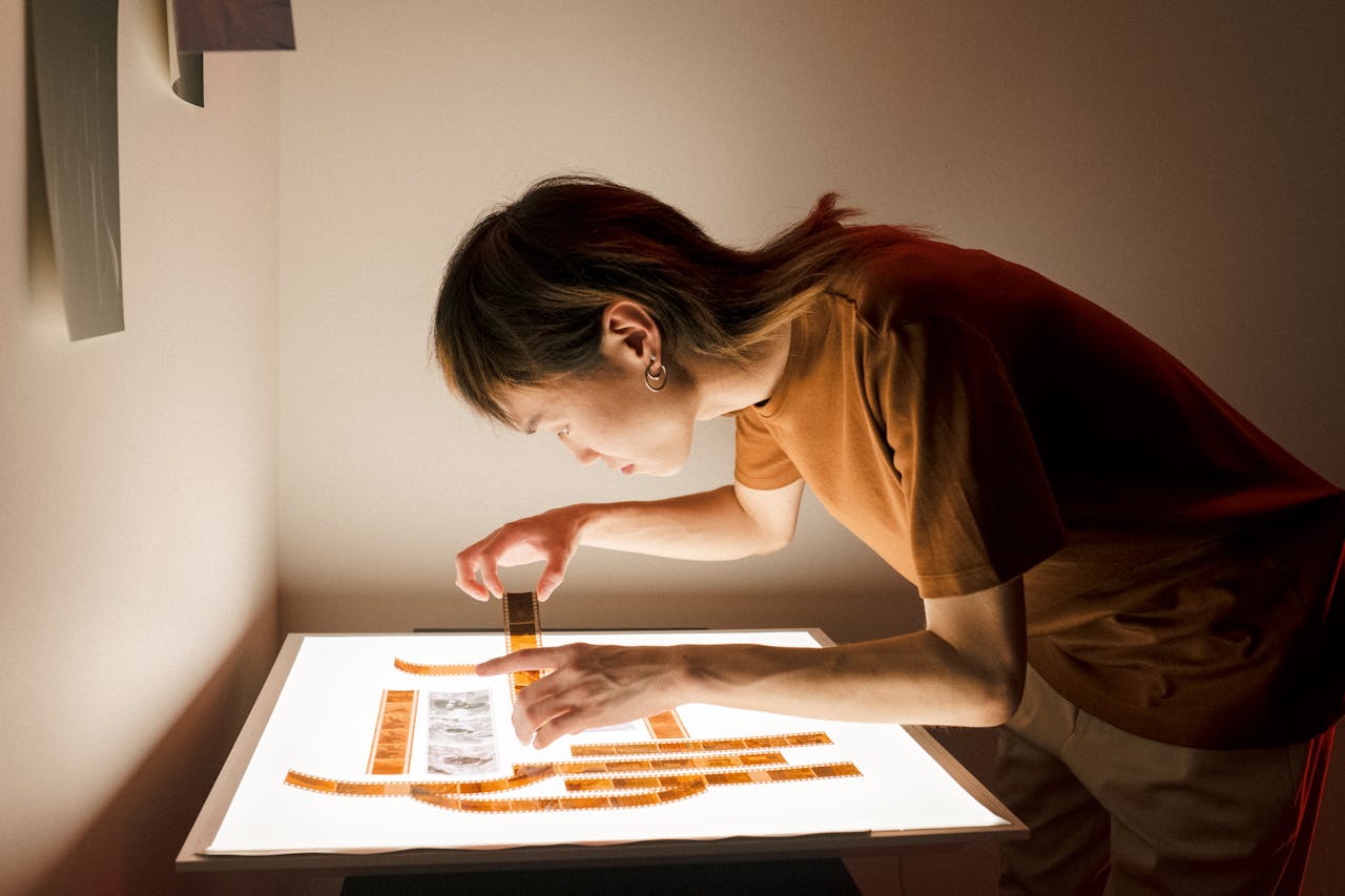 Home A photographer inspects film negatives on a light table in a dimly lit room.